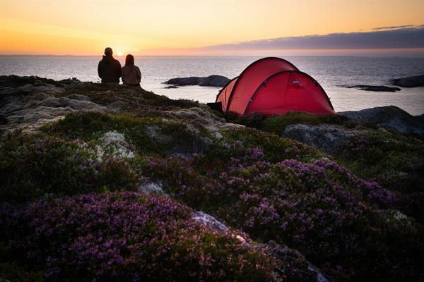 To personer sitter på et svaberg i solnedgangen ved siden av et telt