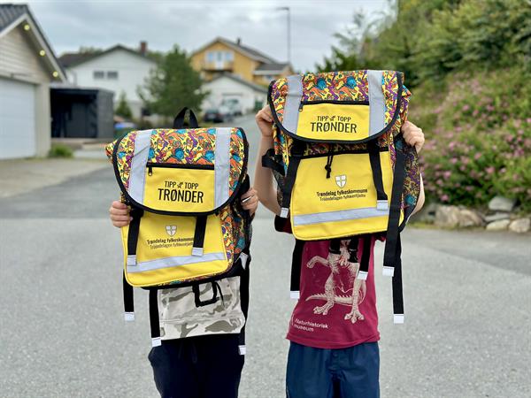 Bildet av to gutter som holder opp en gul skolesekk.