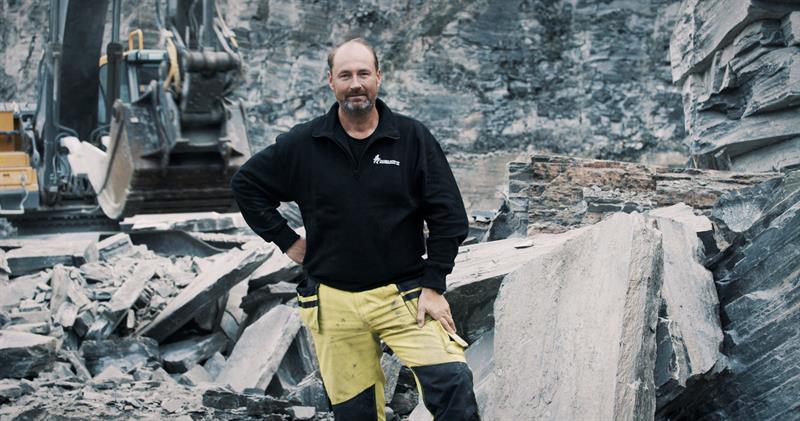 mann i arbeidsklær. Foto Jon Skår En mann står i arbeidsklær foran en gravemaskin