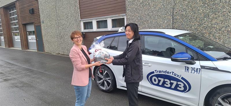 Ordfører Mildrid Kattem Aune deler ut blomster til Jo Kim Bolme Evjen, den første sjåføren i taxiprosjektet i Rindal kommune. Foto: Rindal kommune.